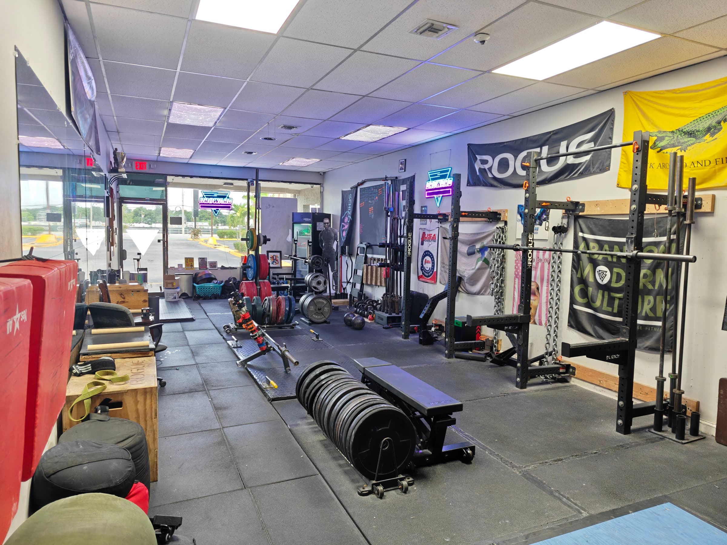 The Broward Strength training floor with racks, platforms, barbells, and strongman equipment